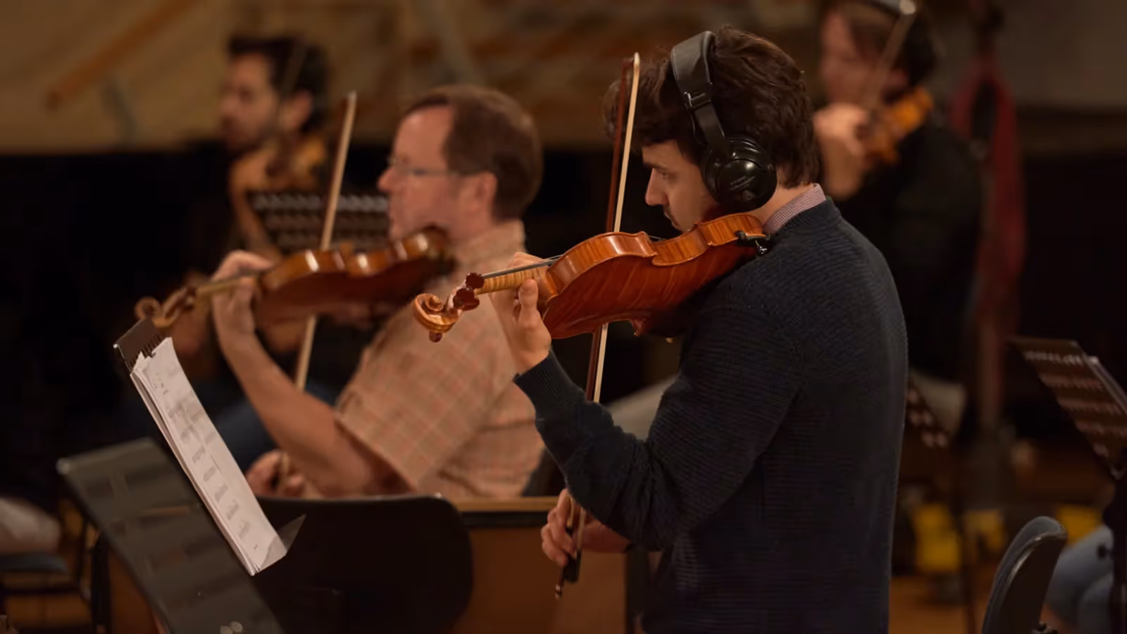 Violinists wearing headphones recording in a wood-panelled hall, from Orchestral Tools’ Berlin Strings product page.